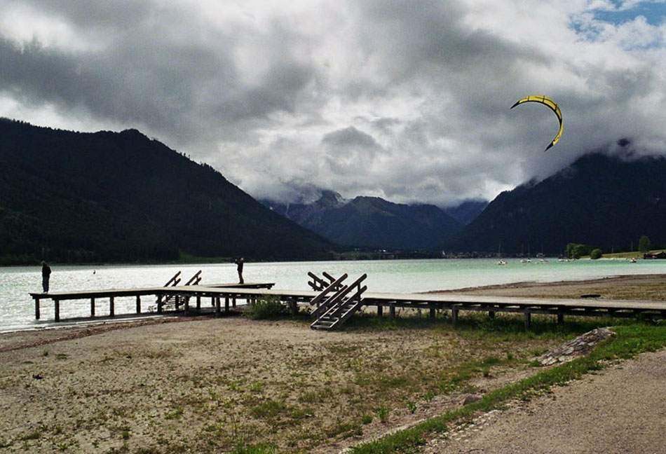 Bergsee mit Holzsteg unter Wolkenhimmel